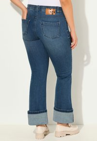 Farkut, joissa on leveä lahje, tummansininen pesu, ommellut yksityiskohdat, kaksi takataskua ja käännetty helma vaaleammasta farkkukankaasta. Nahkainen logo-etiketti vyötäröllä.