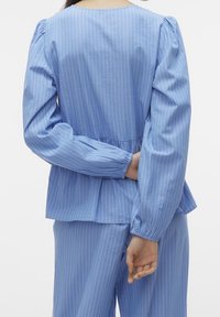 Light blue blouse with vertical white stripes, puffed sleeves, and a peplum hem. Fabric appears soft and lightweight, with gathered accents at cuffs.