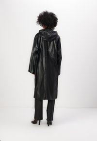 Caban din piele neagră cu glugă, având mâneci lungi și un design până la genunchi, evidențiat prin detalii de cusătură în contrast.