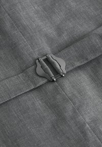 Cinturón de tela gris con una hebilla metálica rectangular que presenta dos lazos acolchados de tela, asegurado sobre una tela gris texturizada a juego.