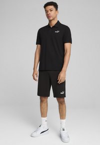 Čierne polo tričko s golierom a krátkymi rukávmi, skombinované s čiernymi šortkami. Na tričku je biele logo Puma, obuté s bielymi teniskami.
