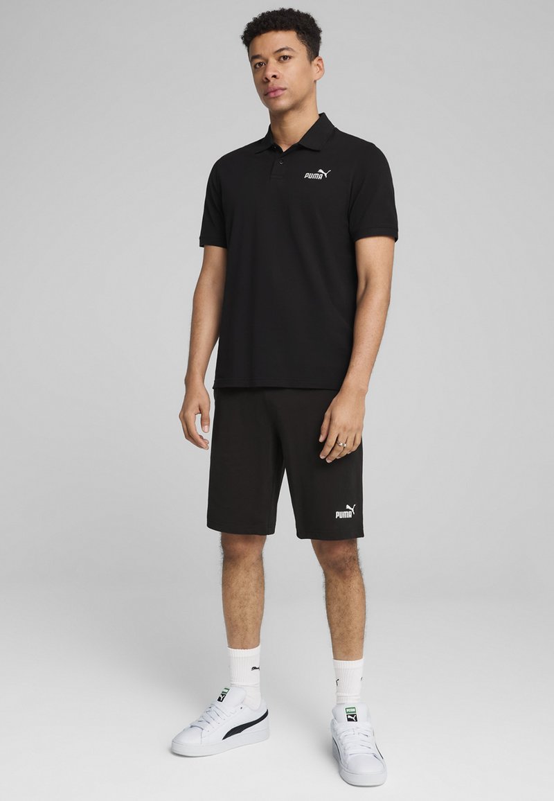 Čierne polo tričko s golierom a krátkymi rukávmi, skombinované s čiernymi šortkami. Na tričku je biele logo Puma, obuté s bielymi teniskami.