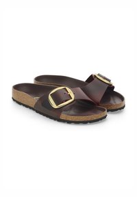 Bruine leren slipper sandalen met grote gouden gespen en kurken voetbedden, weergegeven onder een hoek op een witte achtergrond.