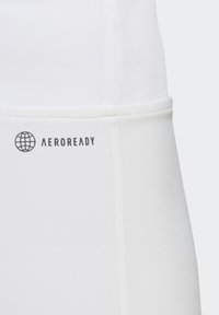 Witte sportkleding van stof met een gladde textuur, voorzien van een zwart "AEROREADY"-logo en een wereldbolontwerp aan de zijkant.