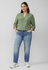 Groene textuur blouse met een V-hals en driekwart mouwen, gecombineerd met lichtblauwe jeans en witte sneakers.