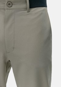 Pantalon gris clair avec une texture lisse, doté d'une fermeture à bouton, de passants de ceinture et d'une taille. Poche latérale visible sur le côté gauche.
