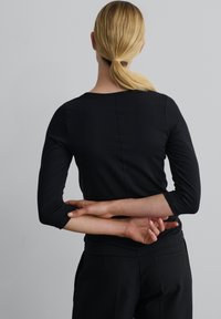 Zwarte langemouwen top met een ronde halslijn en een getailleerd ontwerp. Bevat naadloze stiksels en driekwartmouwen. Gekocht met zwarte broek.