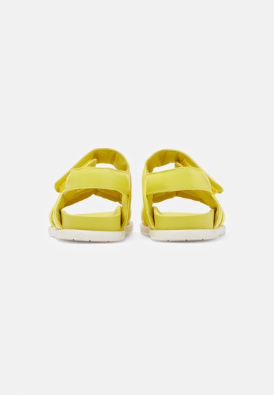 Κίτρινες σαγιονάρες με ρυθμιζόμενες ράντες, ανοιχτή φτέρνα και δάχτυλα, και λευκές σόλες. Λείος υφή με ελάχιστες ραφές.