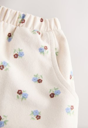 Pantalon en coton avec un tissu doux et léger de couleur crème, présentant de petits motifs floraux bleus et bordeaux. Taille élastique et poche latérale visible.