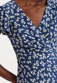 Wrapklänning i marinblått tyg med vita bladmönster. Har korta ärmar, V-ringning och samlingsdetaljer vid midjan. Mjuk textur.