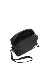 Čierna látková taška so zipsovým uzáverom, zápästným popruh a vnútornými vreckami. Hladká textura s minimálnym brandingom na prednej strane. Kompaktný dizajn.