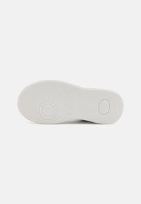 Semelle de chaussure en caoutchouc blanc avec une surface texturée, présentant des motifs de grip circulaires et deux indentations rondes pour une meilleure traction.