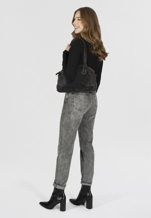 Sac en nylon noir posé sur l'épaule, d'une forme incurvée, avec un accent en métal en forme d'ancre et une seule sangle. Associé à un jean gris taille haute et des bottes noires.