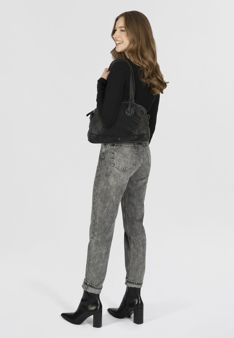 Borsa a spalla nera in nylon con forma curvilinea, accentuata da un ancora in metallo e una sola tracolla. Abbinata a jeans grigi a vita alta e stivali neri.
