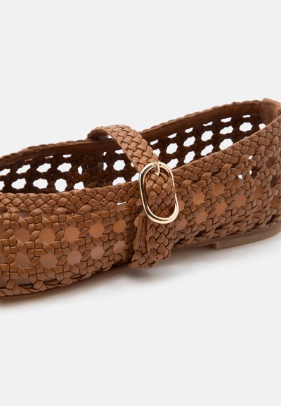 Chaussure plate tissée marron avec une bride et une boucle dorée, avec un design ouvert à motifs en treillis.