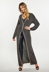 Cardigan lungo, nero e argento, realizzato in materiale a maglia. Presenta un profondo scollo a V, chiusura con bottoni e maniche lunghe con spacchi laterali.