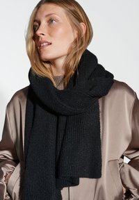 Scarf nero a costine avvolto attorno al collo, realizzato in materiale testurizzato. Indossato con una giacca di satin marrone chiaro.