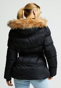 Svart dunjakke med avtakbar hette i kunstpels, belte i midjen og vattert design. Har sidelommer og en glatt, blank tekstur.