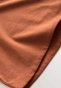 Roestkleurige stof met een zachte, gladde textuur, met een naadloze rand en subtiele draping. Geen patronen of hardware zichtbaar.