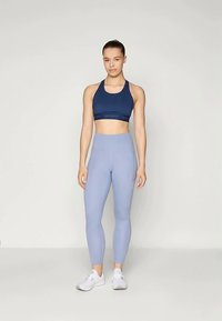 Mornarsko športno modrček z oprijetim dizajnom in logotipnim pasom, združen z svetlo modrimi visokim pasom legicami. Bele športne čevlje dopolnjujejo outfit.