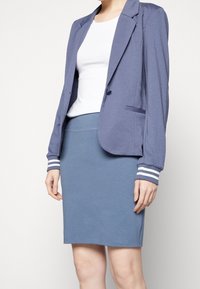 Blazer azul con diseño estructurado, cierre de un botón y puños a rayas, combinado con una falda azul ajustada de tela suave.