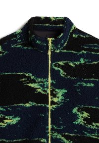 Veste en polaire avec une fermeture éclair intégrale jaune, base noire et bleu foncé, et motifs abstraits verts ressemblant à des nuages.