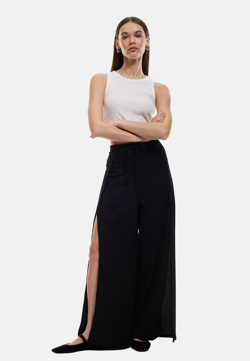 Pantalons larges noirs avec fentes sur les côtés, en tissu doux, associés à un débardeur ajusté à côtes blanc.