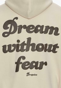 Sweat à capuche beige avec grand texte noir « Rêve sans peur » et une marque plus petite « Dropsize » en dessous au dos.
