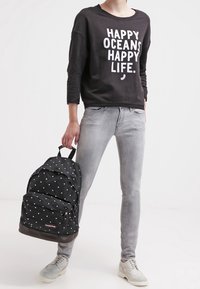 Felpa nera con testo bianco, jeans grigio chiaro, zaino nero a pois bianchi e scarpe grigio chiaro con design perforato.