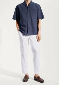 Granatowa koszula na krótki rękaw z kołnierzykiem i na guziki, w zestawieniu z białymi, zwężanymi spodniami i brązowymi butami wsuwanymi.
