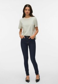 Randig t-shirt med kort ärm i ljusgrått och creme, kombinerad med mörkblå tajta jeans. Svarta spetsiga klackskor fulländar outfiten.