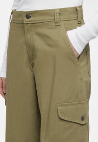 Olijfgroene cargobroek met een gladde textuur, voorzien van voorzakken, een zijzak met klep en een metalen knoop aan de taille.