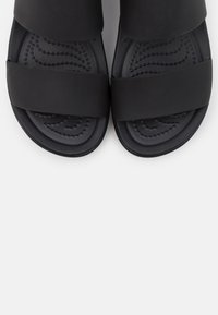 Black sandals with two wide, flat straps, textured footbed featuring curved lines and small raised dots, made from smooth material.