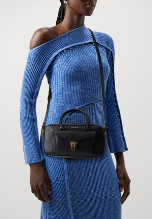 Black leather handbag with a structured shape, gold hardware, and two top handles. Worn with a textured blue knit dress featuring an off-shoulder design.