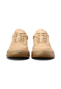 Beige mocka sneakers med perforerat tåbox, platta snörning, gummisula och kontrasterande sömdetalj längs mittsulan.
