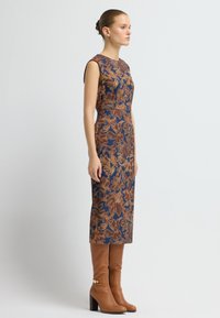 Blommönstrad, marinblå klänning med bruna detaljer, figurnära silhuett, knälång, kombinerad med knähöga bruna stövlar med klack.