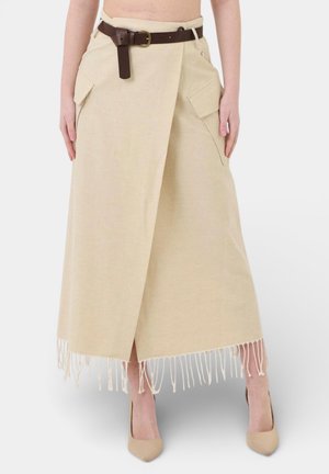 Gonna beige alla caviglia con incrocio frontale, orlo con frange, grandi tasche laterali, cintura marrone, indossata con décolleté beige con punte a punta.