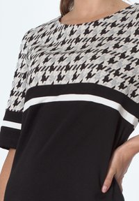 Czarny i szary top z wzorem w szkocką kratę, okrągłym dekoltem i krótkimi rękawami z białym paskiem. Gładka tekstura.