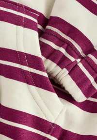 Tissu rayé présentant des couleurs bordeaux et crème, mettant en valeur une texture douce, des détails de couture et un design plié.