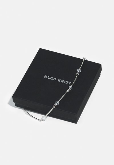 Bracciale d'argento con accenti di cristallo trasparente, posizionato su una scatola nera chiusa. La scatola presenta il nome del marchio "HUGO KREIT" in testo bianco.