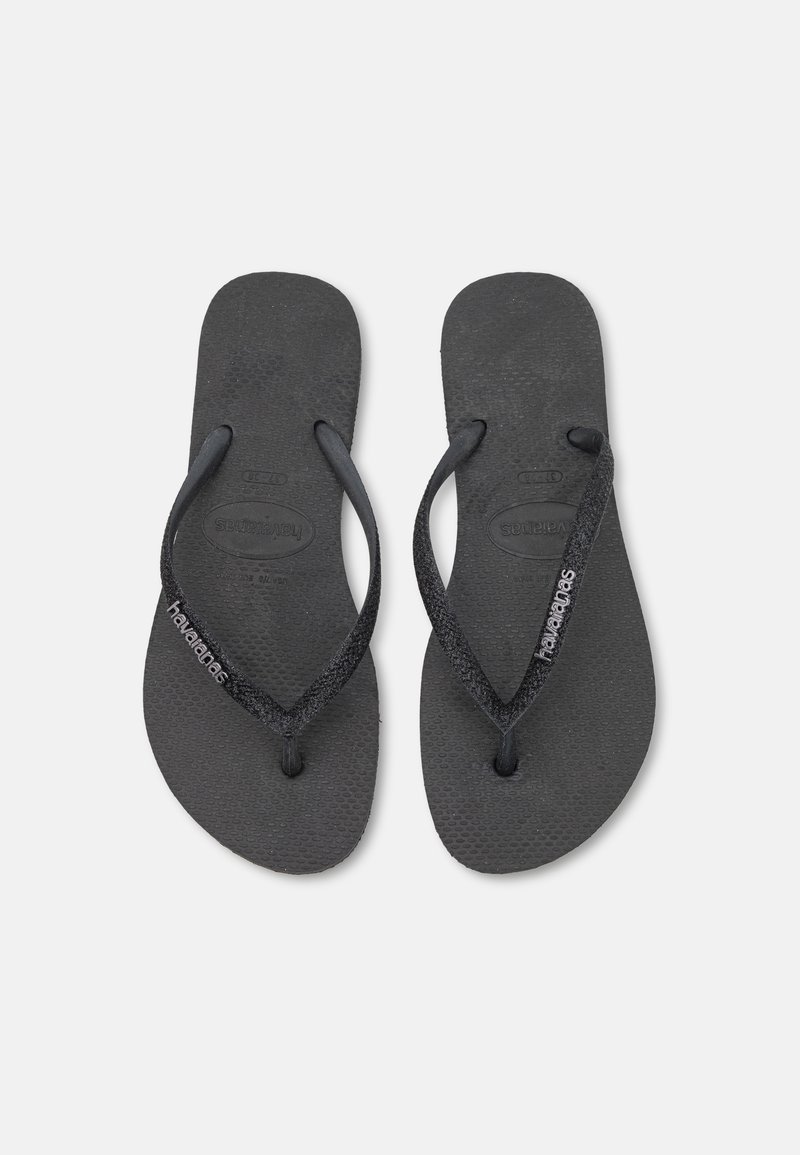 Chinelas de borracha pretas com solas texturizadas e tiras brilhantes. Apresentam a marca Havaianas na tira. Design clássico e minimalista.