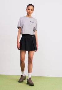 Szara koszulka z krótkim rękawem z logo Nike, zestawiona z czarną plisowaną spódnicą. Obuwie to szare buty sportowe z białymi skarpetkami.