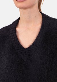Schwarzer Wollpullover mit tiefem V-Ausschnitt, mit weicher, flauschiger Textur und gerippten Details entlang des Kragens.