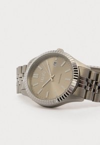 Sølv rustfrit stål ur med en beige urskive, sølv time markører, datovisning og en rillet bezel. Målænke armbånd.