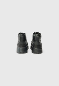 Baskets montantes noires en cuir texturé, avec un col rembourré et une semelle épaisse. Présente des logos à l'arrière et sur les côtés latéraux. Design minimaliste.