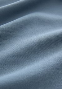 Texturerat tyg i en mjuk blå nyans, med ett fint vävmönster och en jämn yta med mjuka vågor som visar på flexibilitet.