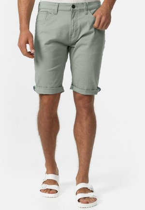 Light green cotton shorts with rolled cuffs, featuring front pockets and a button closure. Worn with white sandals.