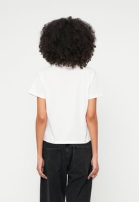 Λευκό βαμβακερό t-shirt με κοντά μανίκια, στρογγυλή λαιμόκοψη και cropped εφαρμογή, συνδυασμένο με μαύρο τζιν παντελόνι φαρδιάς γραμμής με πίσω τσέπες.