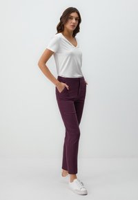 T-shirt blanc à col en V associé à un pantalon ajusté prune, doté de poches latérales et d'une texture lisse et douce. Les chaussures sont blanches avec des accents gris.