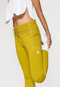 Κίτρινες ελαστικές κολάν με εφαρμοστή σχεδίαση, διαθέτουν φαρδιά μέση, πλαϊνές τσέπες και λεπτομέρεια με λογότυπο. Λείος υφής και στενή εφαρμογή.